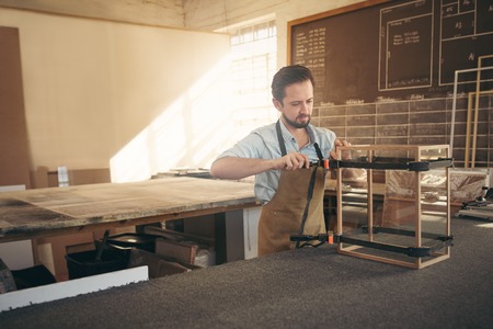 Craftsman carefully manufacturing a glass and wood display case in his workshop