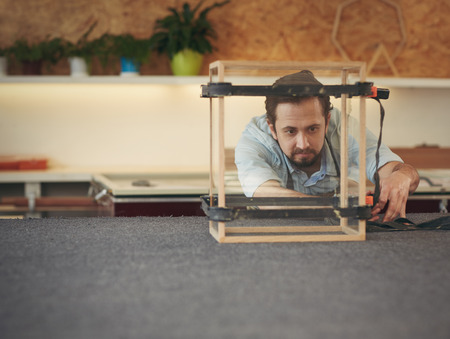 Skilled craftsman carefully inspecting his progress with a manufacturing project he is busy with in...