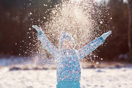 Conceptual shot of a little girl throwing a handful of snow up into the air on a sunny winter's day outdoorsの写真素材