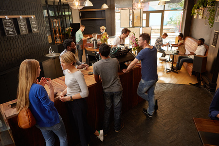 Women and men waiting at a modern coffee shop wooden counter talking and waiting for their coffee ordersの写真素材