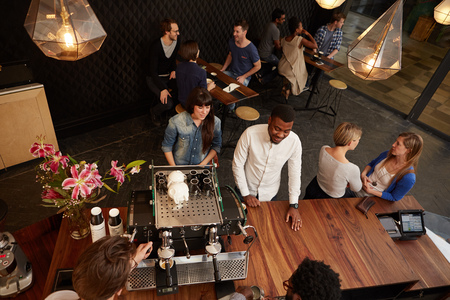 Overhead shot of smiling customers placing their order at the wooden counter of a modern coffee shop