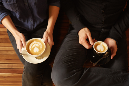 Legs and hands of a hipster wearing jeans and sitting next to each other on a wooden benchの写真素材