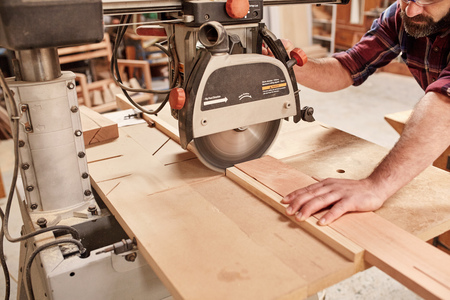Cropped shot of a carpenter using a radial arm circular saw to cut a plank of wood, in his woodwork...