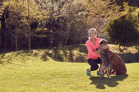 Healthy and active senior woman crousching down to stroke and pet her dogs on a sunny morning outside in her garden, while looking away happily and smilingの写真素材