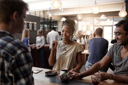 Entrepreneurial African woman smiling and gesturing during a meeting in a busy modern coffee shop with two menの写真素材