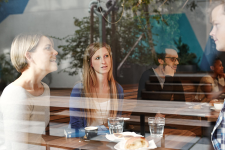 Young woman having coffee with friends in a busy modern cafe, listening carefully while her friends...