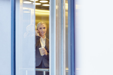 A young businesswoman talking on the phone in elevatorの写真素材