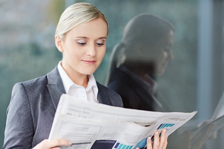 A young businesswoman reading the newpaper outside her officeの写真素材