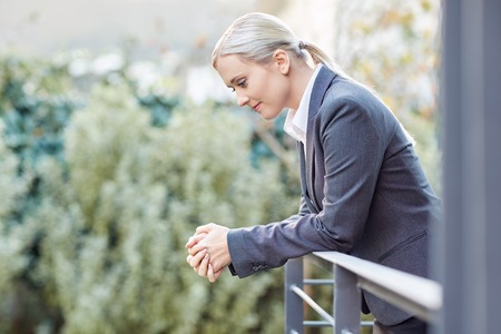 A young businesswoman leaning against the railing of her office balconyの写真素材