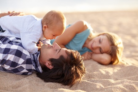 Beautiful family of three lying happily on the beach together for some bonding timeの写真素材