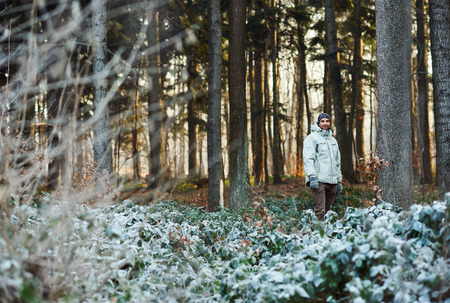 Full length shot of a man in warm clothing standing in tranquil forest with large trees and greenery that has white frost on the leavesの写真素材