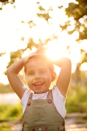 Cute little girl outside smiling happily with early morning sunlight filtering through the treesの写真素材