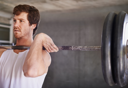 Handsome young man with strong physique lifting heavy weights in a private gymの写真素材