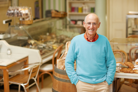 An elderly deli owner standing at the pastry display in his shopの写真素材