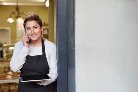 A young deli employee talking on the phone while working on a tablet