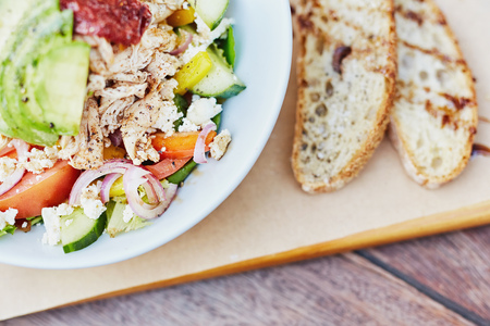 Cropped image of a colourful chicken salad with avocado, sundried tomatoes, yellow peppers, red onion, and feta with two slices of freshly baked bread alongsideの写真素材