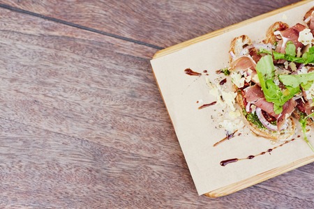 Cropped overhead view of a delicious gourmet bruschetta with fresh parma ham, crsip rocket leaves and petso, presented on a rustic wooden tableの写真素材