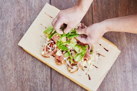 Overhead shot of a chef's hands preparing a delicious bruschetts by adding rockets leaves to the presentationの写真素材