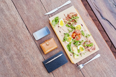 Overhead view of a business person's lunch on their lunch break, of a fresh and healthy salad with their diary, phone and wallet laid out on the tableの写真素材