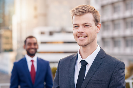 Portrait of a smiling businessman with a colleague in the background standing in the cityの写真素材