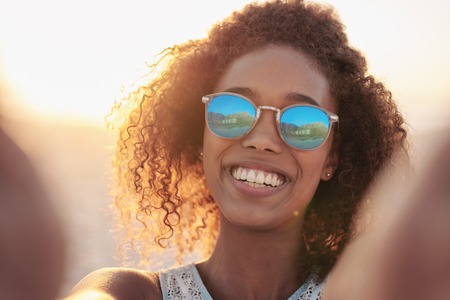 Portrait of a smiling woman wearing sunglasses at the beachの写真素材