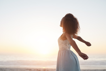 Beautiful young woman standing on a beach with her arms raised in the air