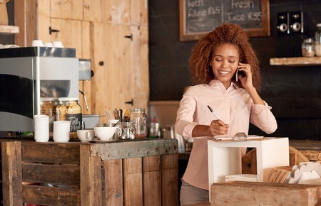 Attractive young woman talking on the phone while working in cafeの写真素材