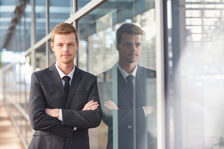 Portrait of a confident and successful businessman standing with his arms crossed outside leaning against the glass windows of a modern office buildingの写真素材