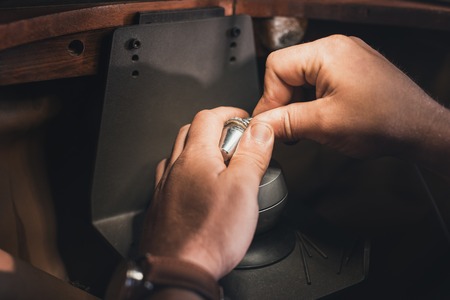 Closeup of a jeweler using tools to shape a silver ring while working at a bench in his workshop