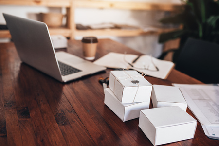 Closeup of a desk with a laptop, paperwork, scissors, string and boxes being prepared for shipping to customersの写真素材