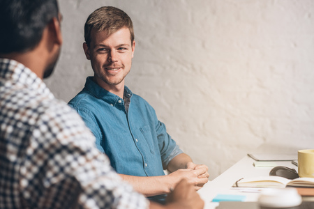 Two smiling designers discussing work while sitting together at a desk in an officeの写真素材