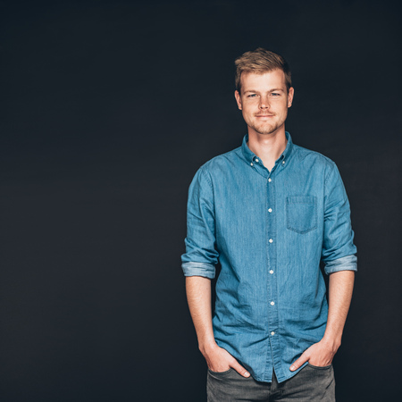 Studio portrait of a smiling and confident young entrepreneur standing with his hands in his pockets in front of a dark backgroundの写真素材