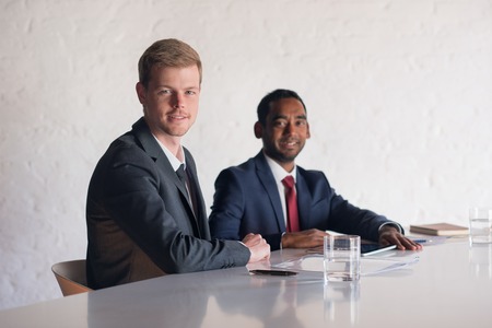 Portrait of two smiling young businessmen sitting together,at a table with documents in a modern boardroomの写真素材