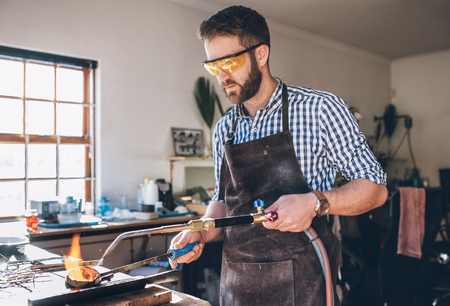 Focused jeweler using  a torch to melt metal in a crucible while working in his jewelry design studioの写真素材