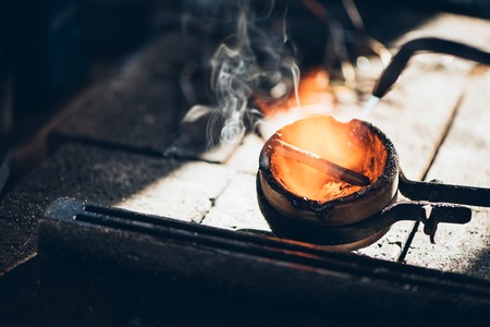 Closeup of a jeweler using  a torch to melt a metal ingot in a crucible while working in his jewelry design studioの写真素材