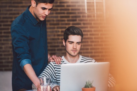 Young gay couple talking together while using a laptop at a table at homeの写真素材