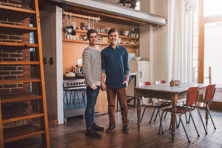 Portrait of an affectionate young gay couple standing side by side together in their loft apartmentの写真素材