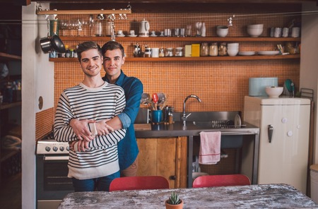Portrait of an affectionate young gay couple standing arm in arm together in their kitchenの写真素材