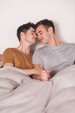 Affectionate young gay couple kissing while lying in bed tegother in the morning
