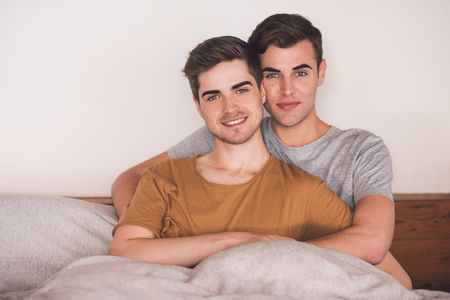 Portrait of an affectionate young gay couple lying arm in arm together in bed in the morning