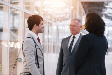 Diverse group of smiling businesspeople talking together while standing in the lobby of a modern office buildingの写真素材