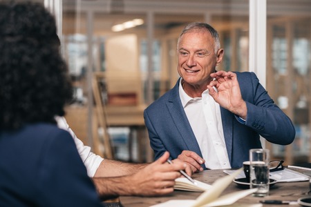 Mature businessman talking with young staff members while sitting together at a table in an office boardroomの写真素材