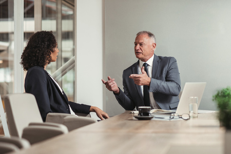 Mature businessman and young work colleague discussing business while sitting together at a table in an office boardroomの写真素材