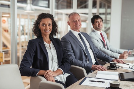 Portrait of a diverse group of smiling businesspeople sitting in a row together at a table in an...