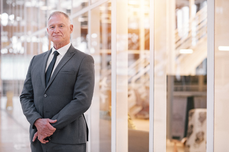 Portrait of a confident mature businessman in a suit standing in the lobby of a modern office buildingの写真素材
