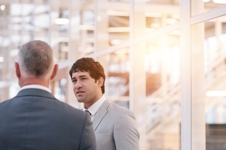 Focused young businessman talking to a mature manager while standing together in the lobby of a modern office buildingの写真素材