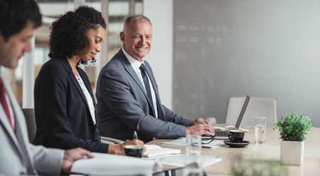 Portrait of a smiling mature businessman sitting at a boardroom table with a diverse group of colleaguesの写真素材