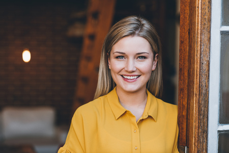 Portrait of an attractive young blonde woman smiling while standing at the door to her modern loft apartmentの写真素材