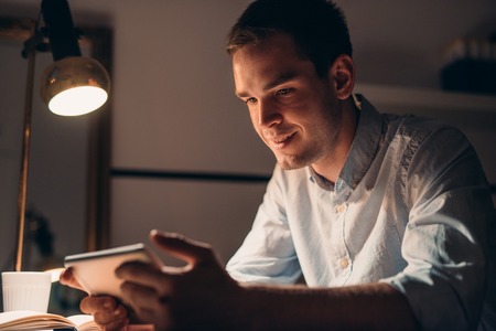 Smiling young businessman working using a tablet late at night