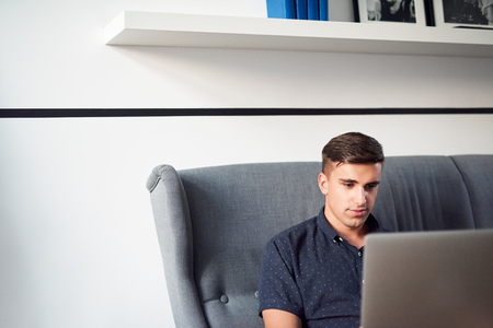 Young man relaxing on sofa at home using a laptopの写真素材